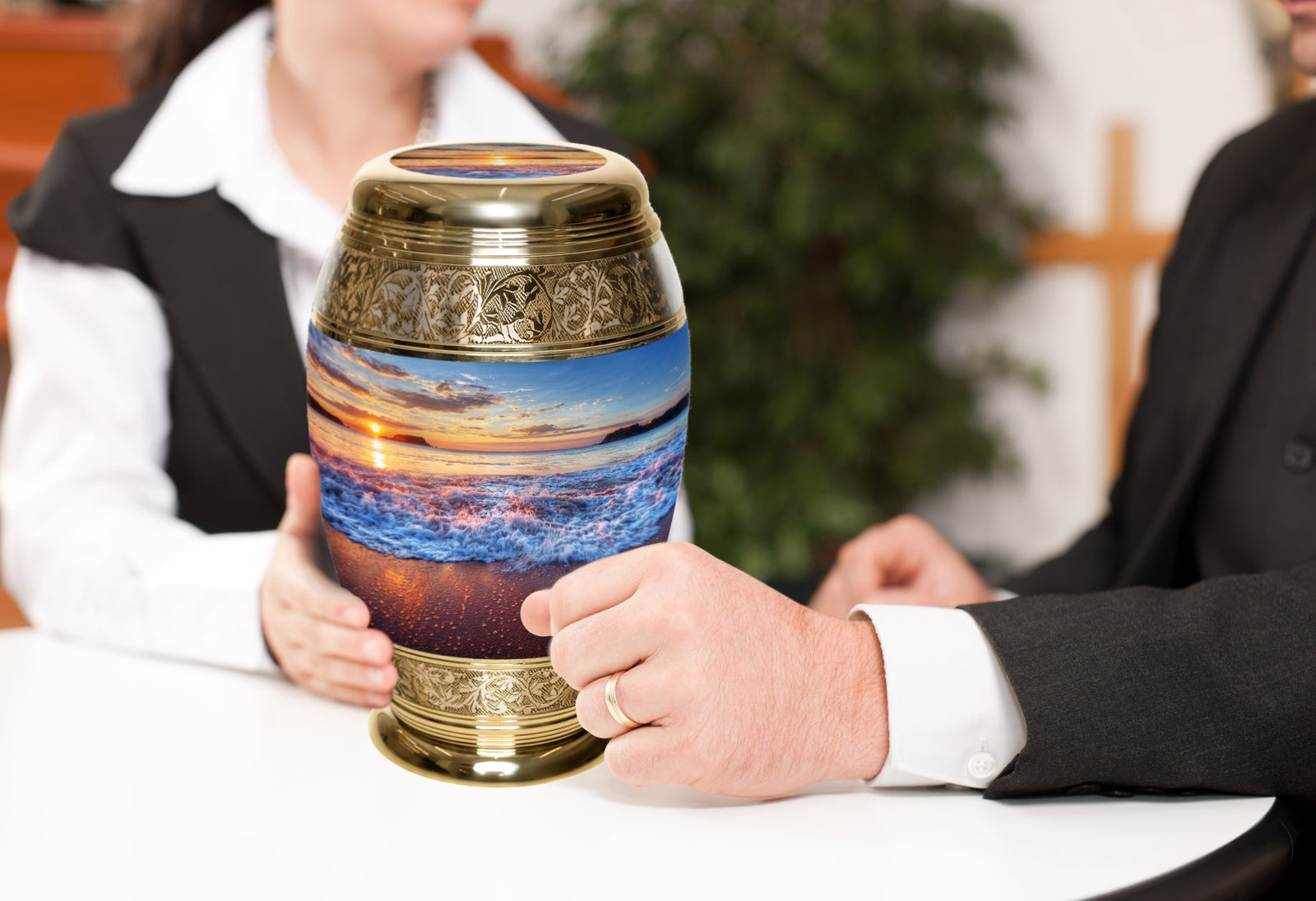 Elegant metal cremation urn with beach sunset design held by two people at a table