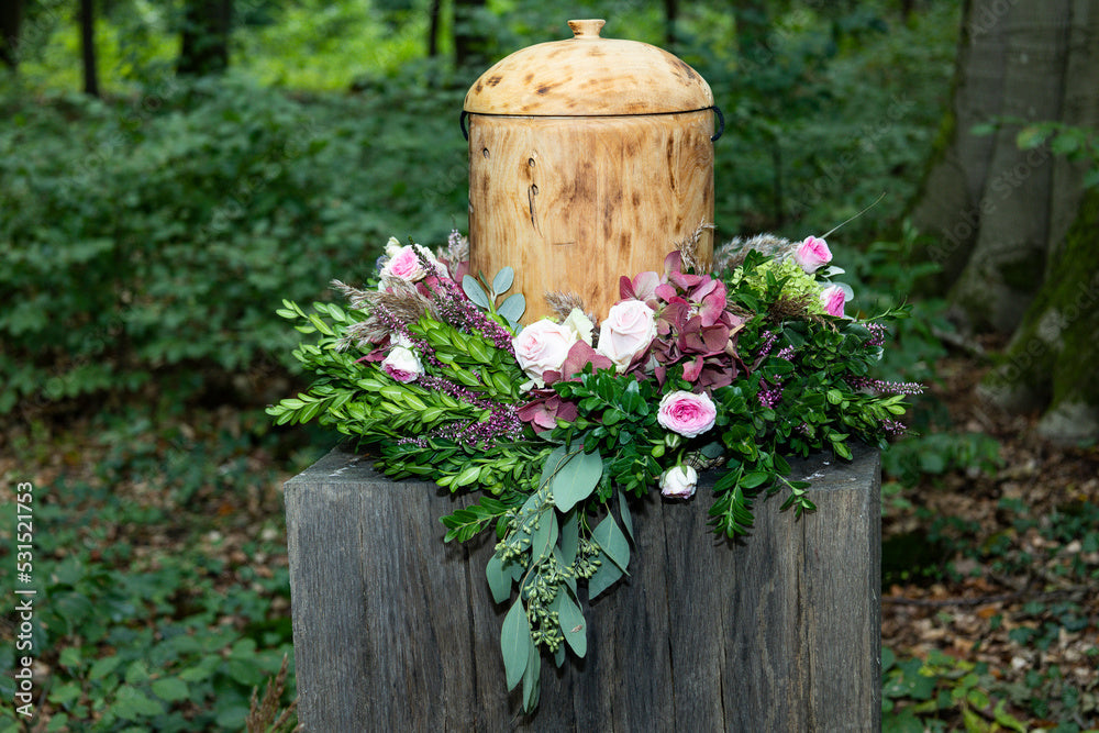 Wooden cremation urn with a floral wreath on a pedestal in a natural forest setting