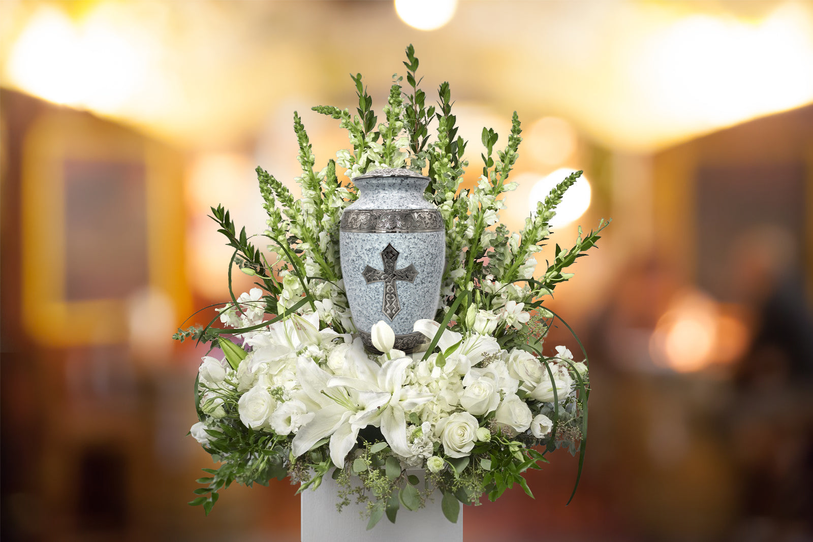 Metal cremation urn with cross detail surrounded by white flowers at memorial service.