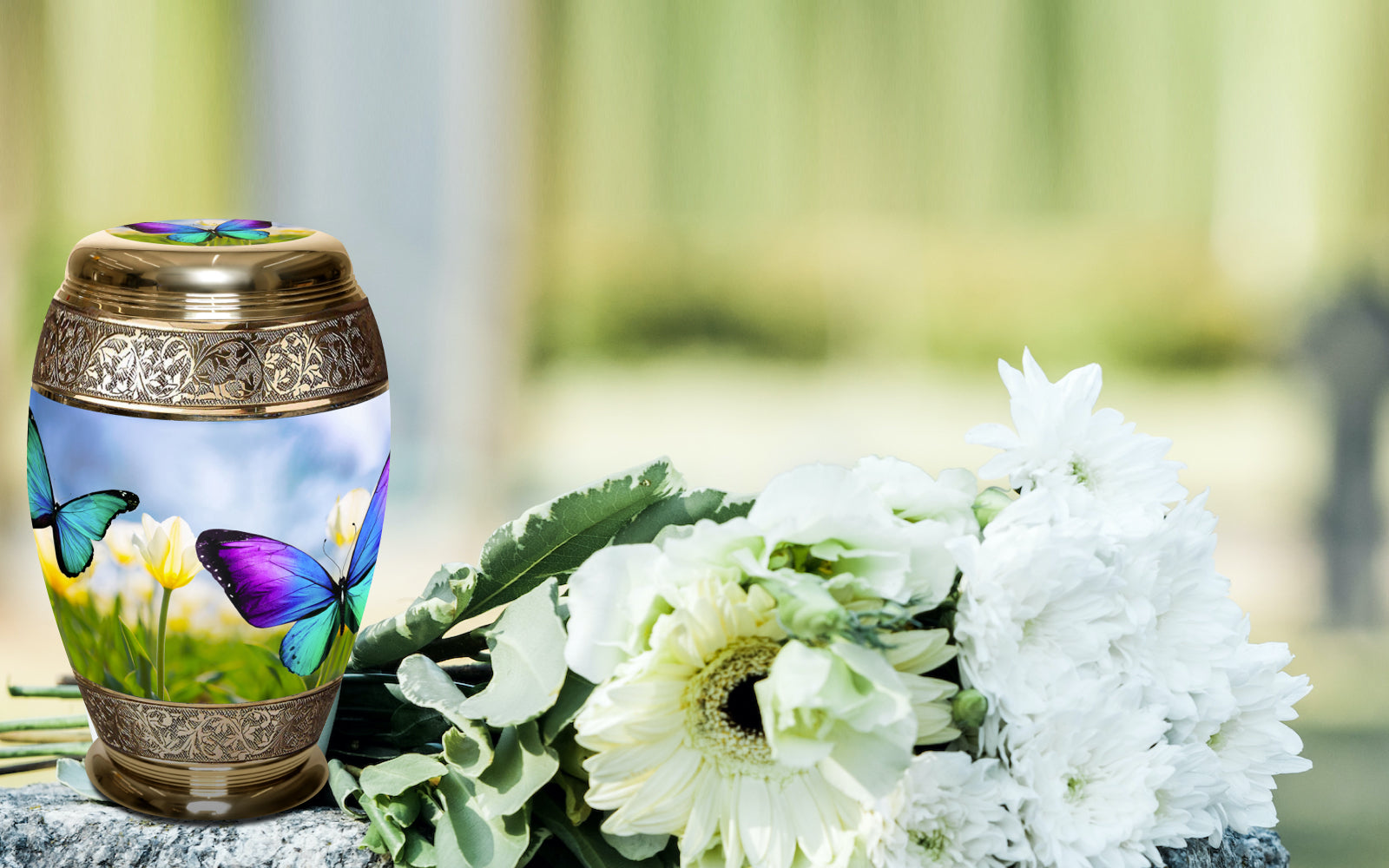 Metal cremation urn with butterfly and flower design beside white floral bouquet outdoors